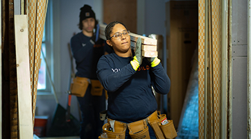 YouthBuild students carry lumber inside house under construction