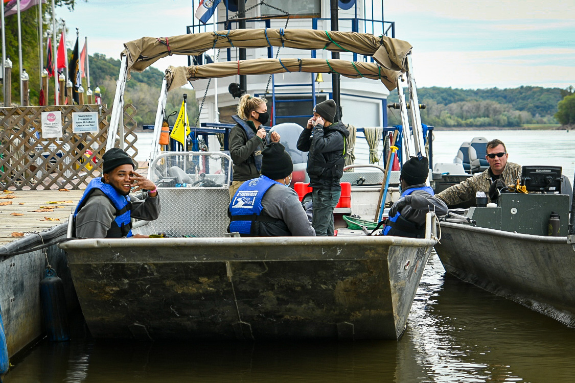 Students in YouthBuild USA apparel sitting on a boat. One is facing the camera while the others interact with each other.